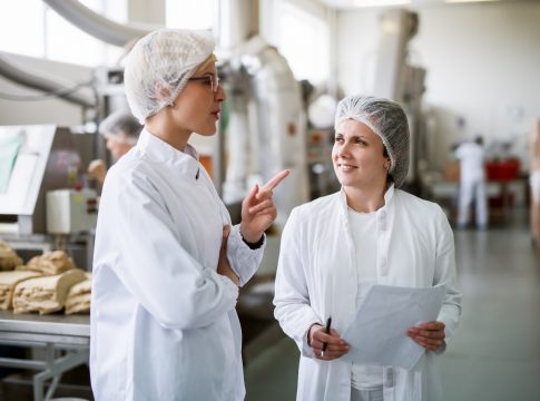 Two female workers discussing while standing in food factory. Qué es APPCC