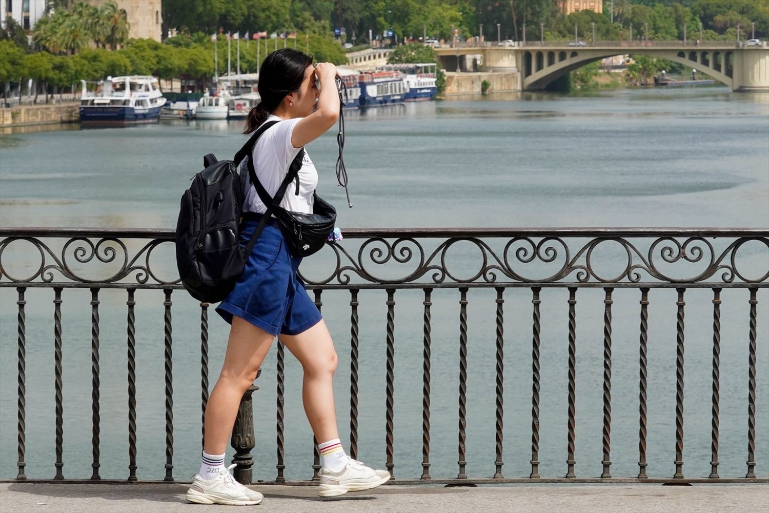 Una persona paseando por el Puente de Triana se protege la cara el día en que la capital está en alerta naranja por el calor
