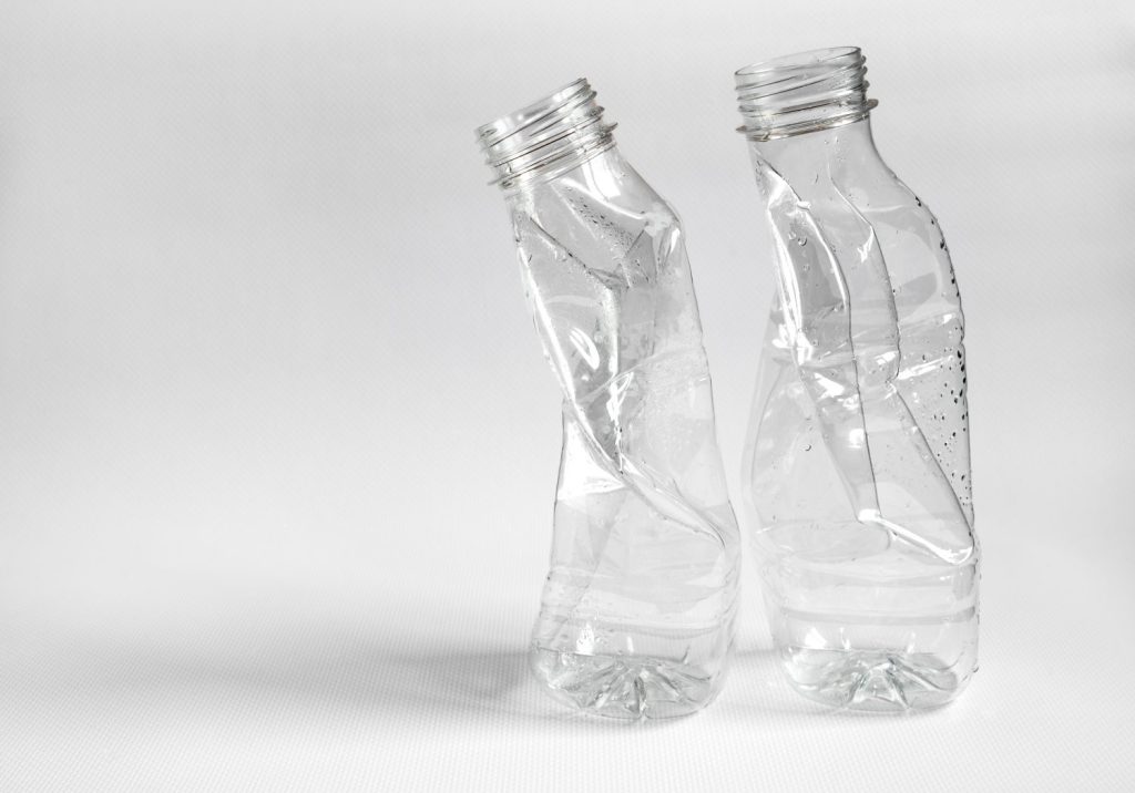 dos botellas de plastico trituradas preparadas para reciclar sobre un fondo claro