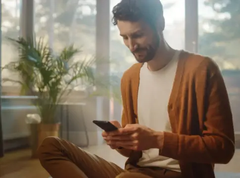 man-using-smartphone-home-does-remote-work-handsome-smiling-male-sitting-floor-works-with-papers-documents-brainstorms-creative-project-with-online-research-sunny-living-room