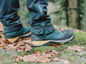 Primer plano de botas de senderismo rodeadas de hojas caídas en un sendero cubierto de musgo en el bosque durante el otoño.