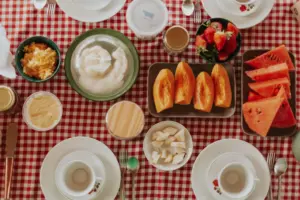 Desayuno vibrante con frutas frescas, pasteles y productos lácteos sobre un mantel a cuadros.