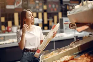 Joven eligiendo una baguette fresca en el pasillo de panadería de un supermercado moderno.