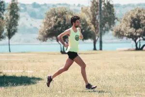Joven enérgico corriendo junto al lago en un día soleado, abrazando el fitness y la naturaleza.