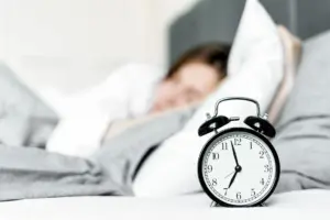 Un reloj despertador retro está junto a una mujer durmiendo en un acogedor ambiente de dormitorio.