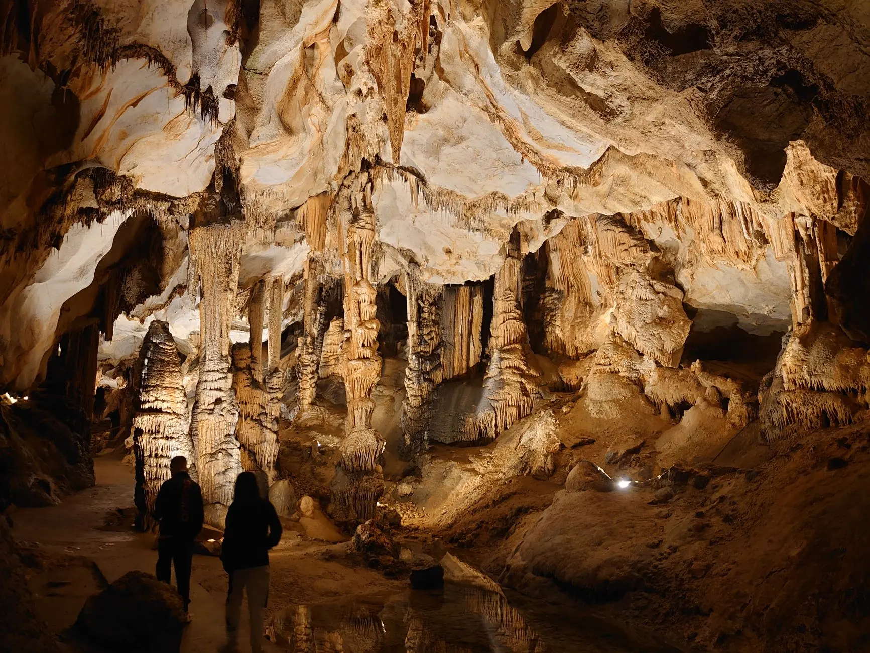 Estalactitas y estalagmitas dramáticas en una cueva de limestone con dos personas explorando.