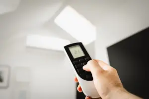 Acercamiento de un hombre usando un control remoto para controlar el aire acondicionado en interiores.