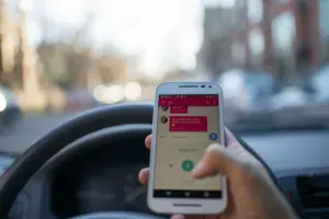 Una persona enviando mensajes en un smartphone mientras conduce un automóvil en la ciudad, ilustrando la conducción distraída y el uso de la tecnología.