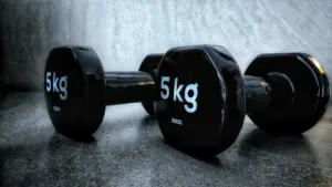 Primer plano de mancuernas negras de 5 kg sobre una superficie oscura texturizada, que muestra equipos de entrenamiento físico y de fuerza.