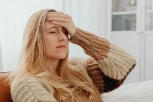 Primer plano de una mujer con dolor de cabeza, mano en la frente, en un entorno cómodo.