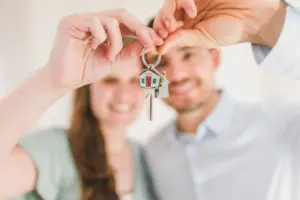 Joven pareja sosteniendo las llaves de su nuevo hogar, simbolizando un nuevo comienzo y una inversión en bienes raíces.
