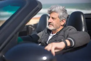 Un hombre mayor disfrutando de un viaje por una pintoresca carretera costera en un coche descapotable.