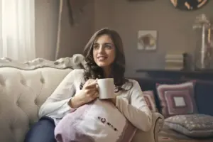 Mujer relajándose con una taza de café en un sofá en una sala de estar acogedora.