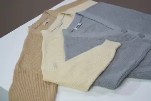 Disposición de cárdigans beige, crema y gris sobre una superficie blanca. Perfecto para compras en línea y catálogos de moda.