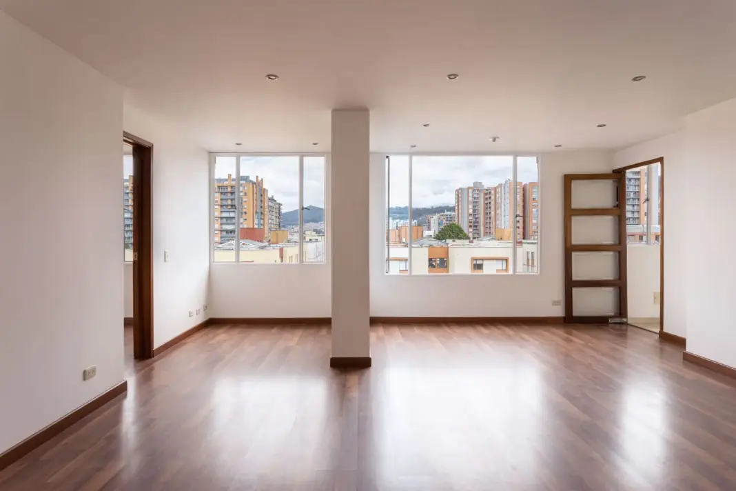 pexels-9826456 Un interior de apartamento vacío y luminoso que muestra grandes ventanas y suelo de madera.