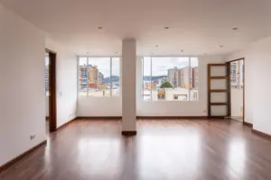 Un interior de apartamento vacío y luminoso que muestra grandes ventanas y suelo de madera.