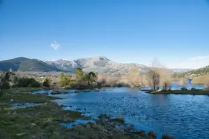 Snow-capped mountains overlook a serene lake under a clear sky