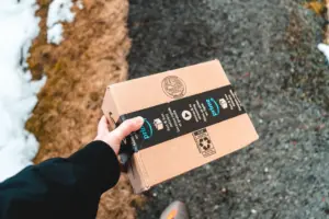 Una persona sosteniendo un paquete de cartón de Amazon Prime en una acera urbana nevada.