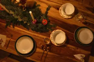 Configuración de mesa navideña cálida y acogedora con velas y decoración de pino sobre superficie de madera.