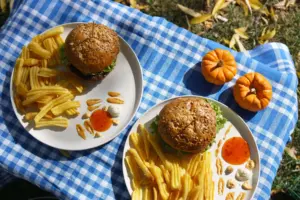 Deliciosas hamburguesas y papas fritas en un picnic con mini calabazas, celebrando el otoño al aire libre.
