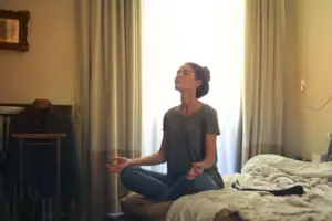 Mujer adulta practicando meditación en su cama rodeada de una atmósfera tranquila en el dormitorio.