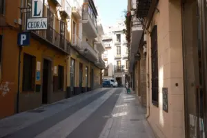 Explora una calle estrecha y tranquila en Granada, flanqueada por edificios pintorescos y una atmósfera serena.