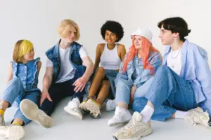 Un grupo diverso de adolescentes sentados juntos en interiores, vistiendo conjuntos de denim modernos y expresando alegría.