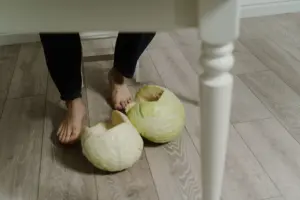 Primer plano de pies descalzos al lado de repollos en un suelo de madera interior.